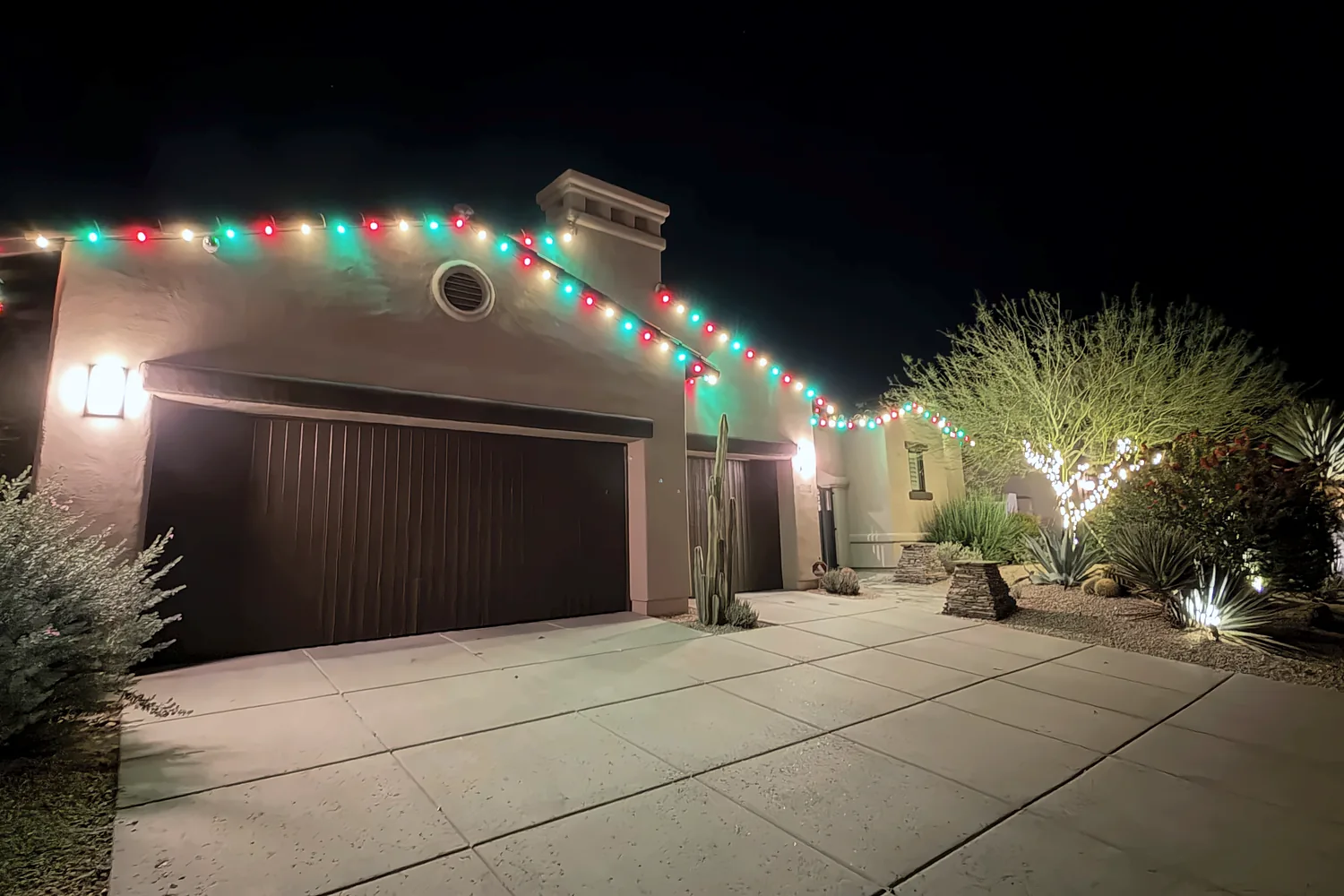 Red and green C9 roofline over a garage with a light-wrapped tree