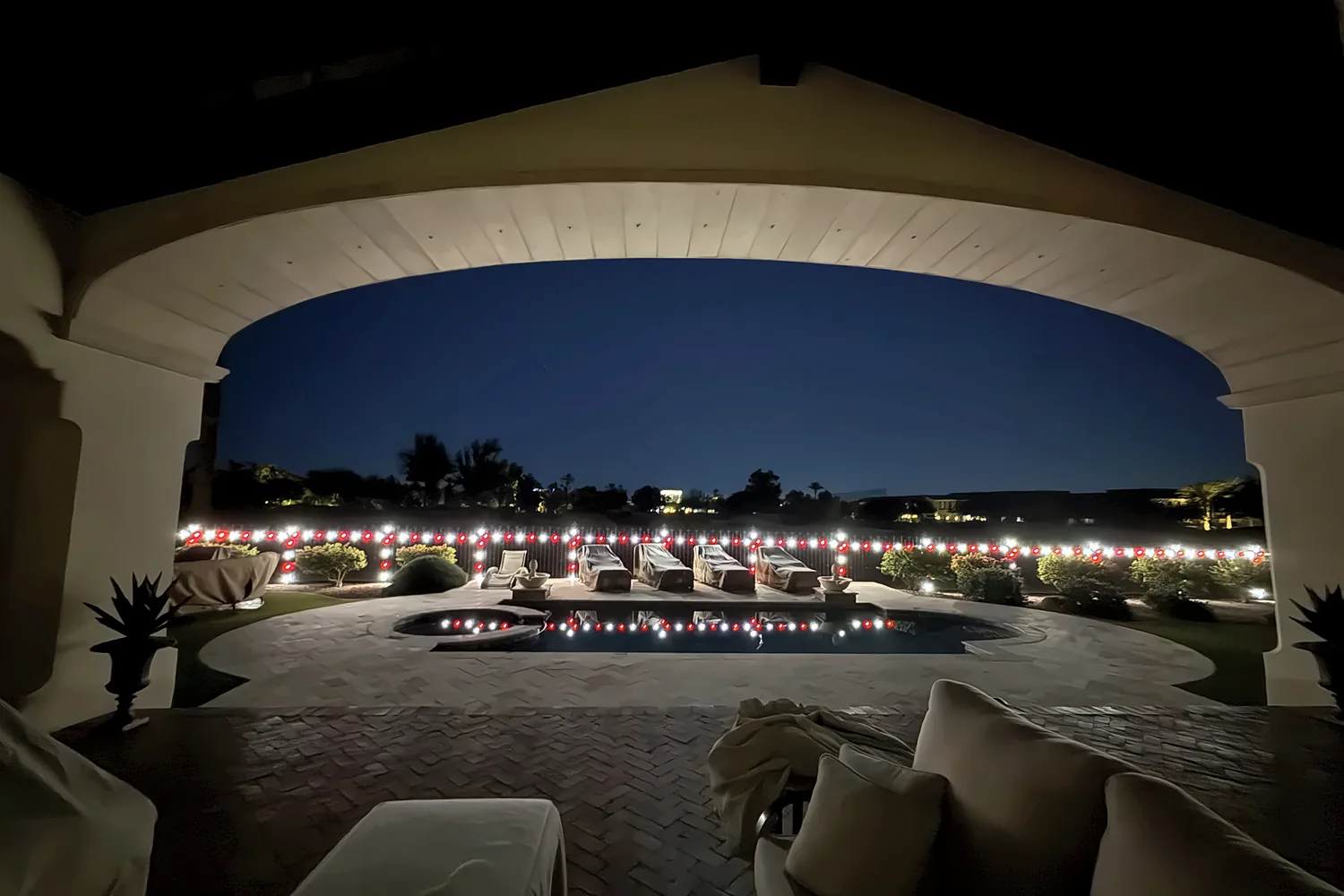 Red and white C9 lights around a pool seen through a patio arch